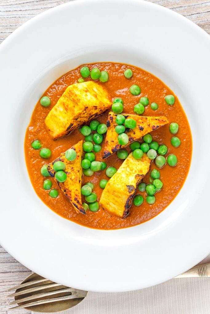 Portrait overhead image of a matar paneer curry in a masala sauce served in a white bowl