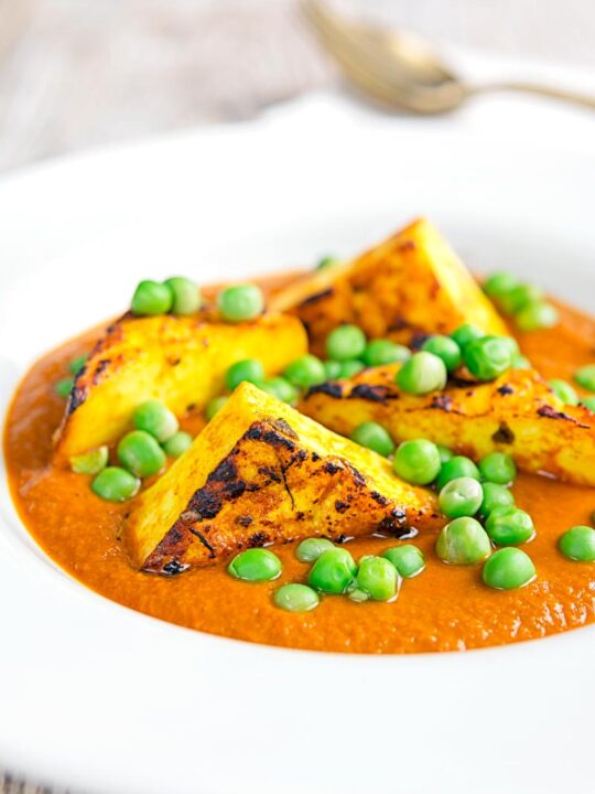Portrait image of a matar paneer curry in a masala sauce served in a white bowl