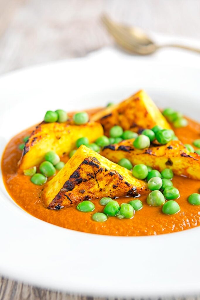 Portrait image of a matar paneer curry in a masala sauce served in a white bowl