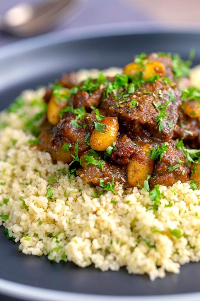 Portrait image of a rich Moroccan Lamb tagine with almonds in a date sauce served on buttered couscous