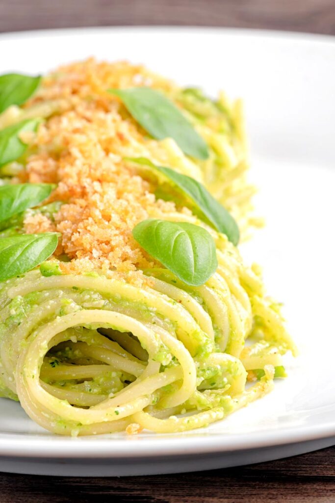 Portrait image of pea pesto pasta with toasted bread crumbs and fresh basil leaves elegantly presented on a white plate