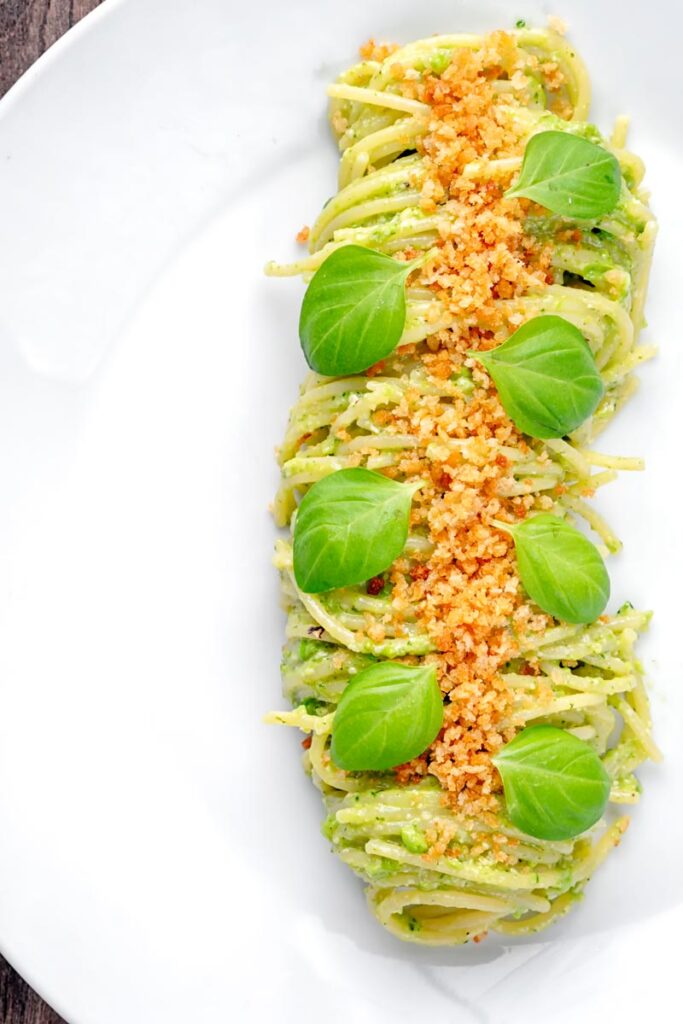 Portrait overhead image of pea pesto pasta with toasted bread crumbs and fresh basil leaves elegantly presented on a white plate