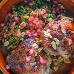 Portrait overhead image of pomegranate molasses glazed chicken thighs served with Israeli couscous and pomegranate seeds