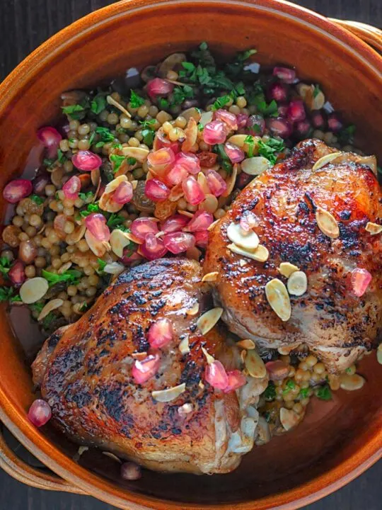 Portrait overhead image of pomegranate molasses glazed chicken thighs served with Israeli couscous and pomegranate seeds