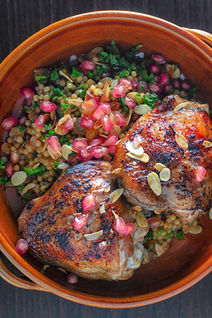 Portrait overhead image of pomegranate molasses glazed chicken thighs served with Israeli couscous and pomegranate seeds