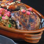 Portrait close up image of pomegranate molasses glazed chicken thighs served with Israeli couscous and pomegranate seeds