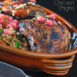 Portrait close up image of pomegranate molasses glazed chicken thighs served with Israeli couscous and pomegranate seeds with text overlay