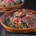 Portrait image of pomegranate molasses glazed chicken thighs served with Israeli couscous and pomegranate seeds
