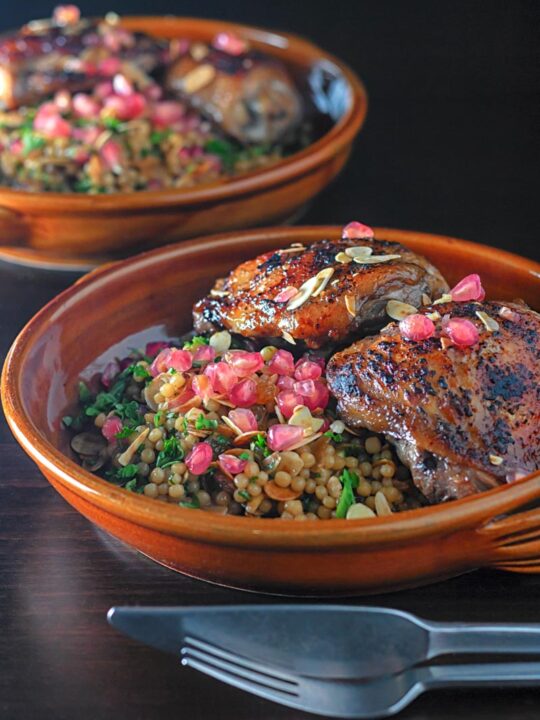 Portrait image of pomegranate molasses glazed chicken thighs served with Israeli couscous and pomegranate seeds