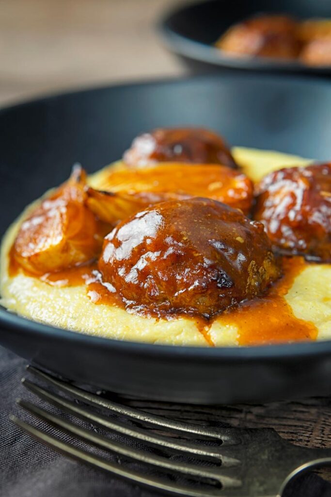 Portrait image of pork meatballs in bbq sauce served on polenta in a black bowl