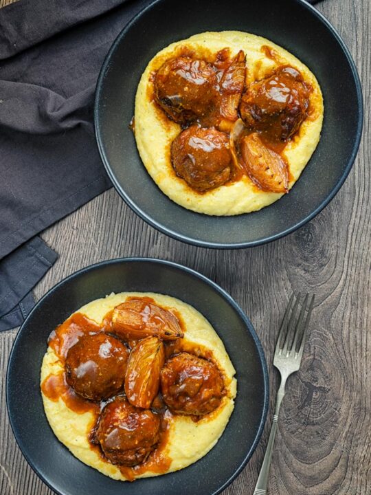 Portrait overhead image of pork meatballs in bbq sauce served on polenta in a black bowls