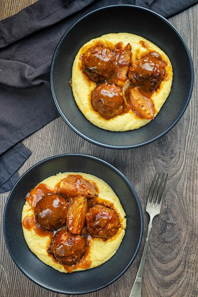 Portrait overhead image of pork meatballs in bbq sauce served on polenta in a black bowls