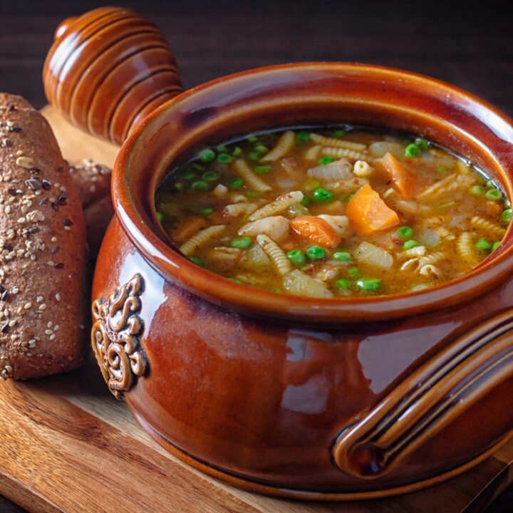 Square image of soupe au pistou served in a large glazed earthenware bowl with bread on the side