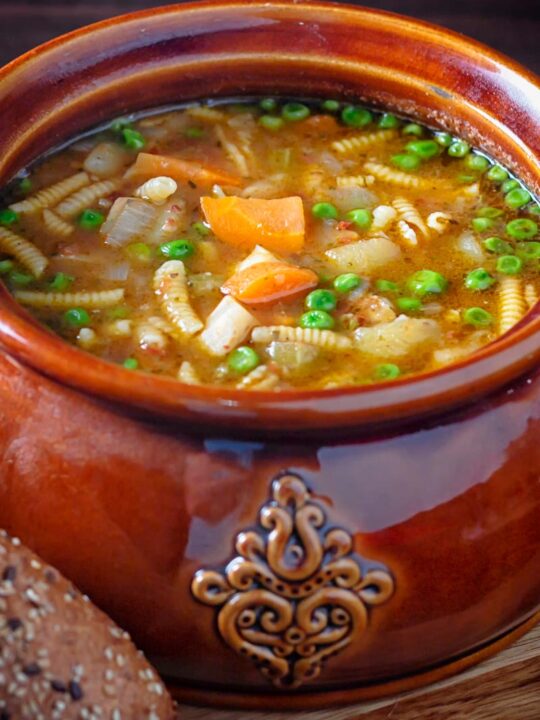 Portrait image of soupe au pistou served in a large glazed earthenware bowl with bread on the side