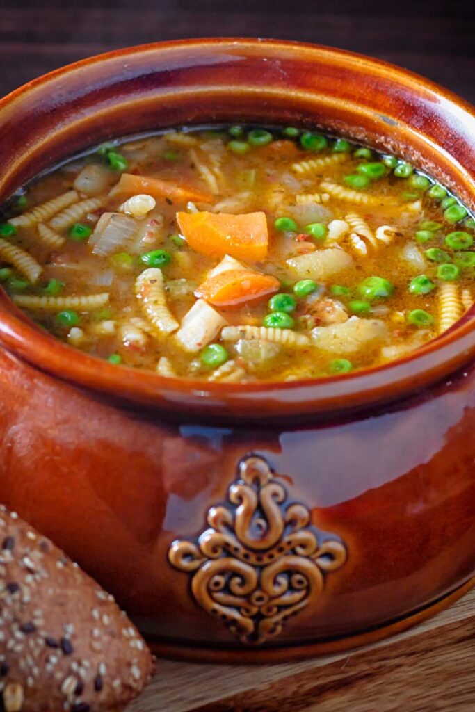 Portrait image of soupe au pistou served in a large glazed earthenware bowl with bread on the side