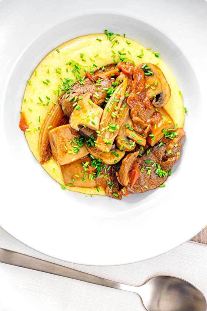 Portrait overhead image of a mushroom ragu served on polenta porridge with shipped chives served in a white bowl