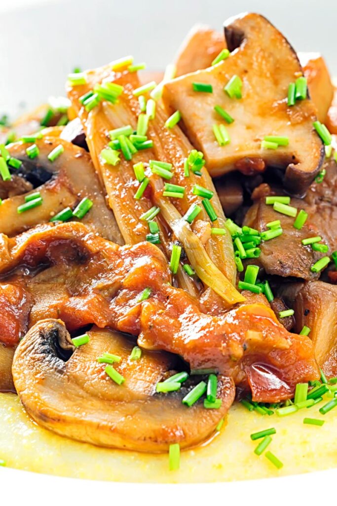 Portrait close up image of a mushroom ragu served on polenta porridge with shipped chives served in a white bowl