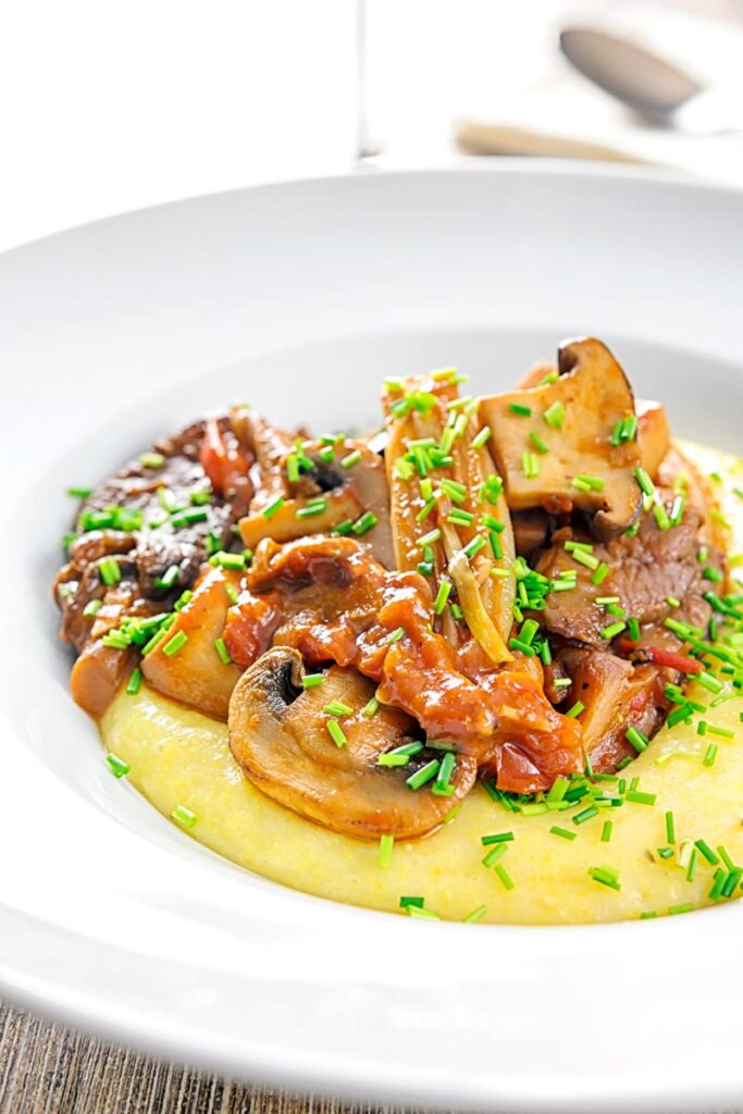 Portrait image of a mushroom ragu served on polenta porridge with shipped chives served in a white bowl