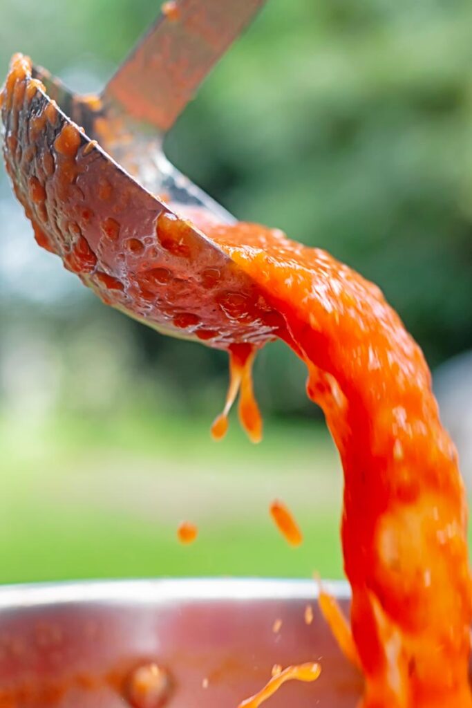 Portrait image of roasted tomato passata being poured from a ladle