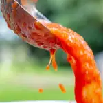 Portrait image of roasted tomato passata being poured from a ladle with text overlay