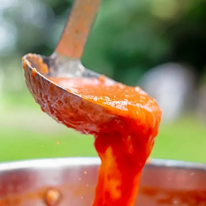 Square image of roasted tomato passata being poured from a ladle