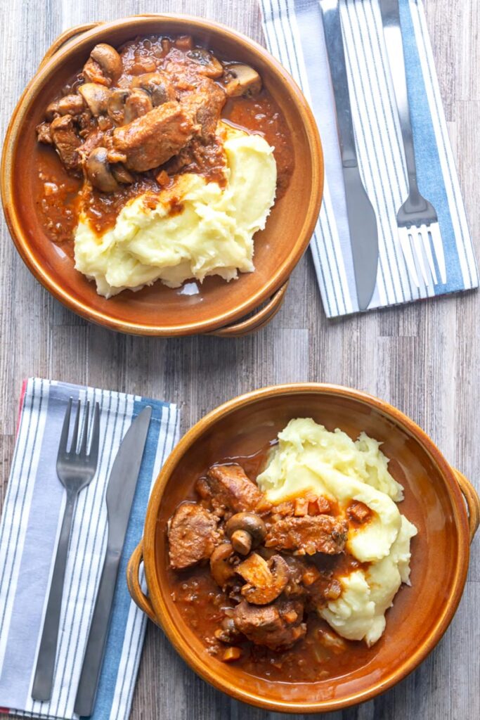 Portrait overhead image of a tomato based wild boar stew with mushrooms served in earthenware bowls with mashed potatoes