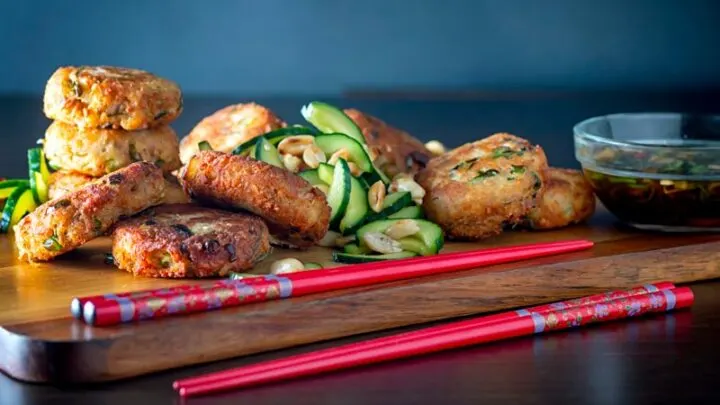 Landscape image of spicy Thai tuna fish cakes served with a cucumber and peanut salad and a dipping sauce.