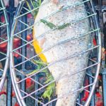 Portrait image of a whole trout being cooked on a BBQ in a fish basket