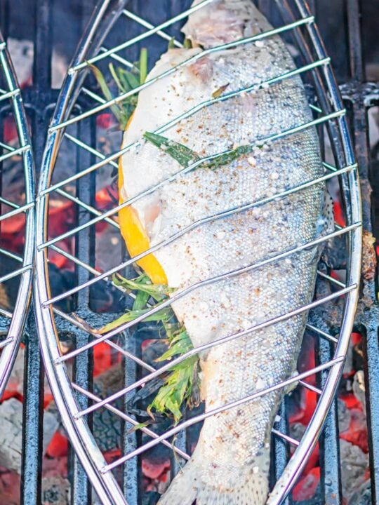 Portrait image of a whole trout being cooked on a BBQ in a fish basket