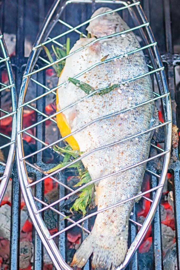 Portrait image of a whole trout being cooked on a BBQ in a fish basket