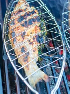 Portrait image of a whole trout that has been cooked on a BBQ in a fish basket