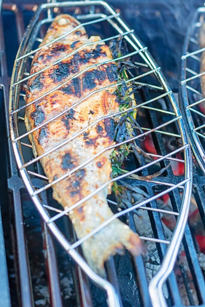 Portrait image of a whole trout that has been cooked on a BBQ in a fish basket