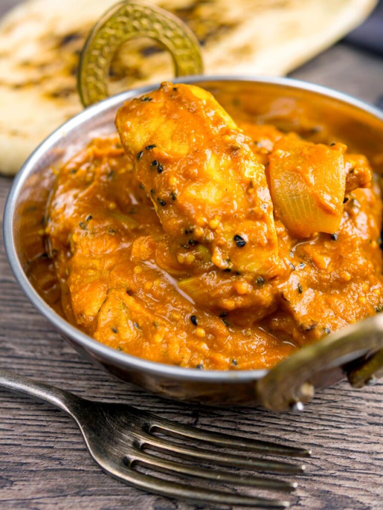 Portrait image of a chicken jalfrezi curry served in a tarnished copper covered karahi bowl