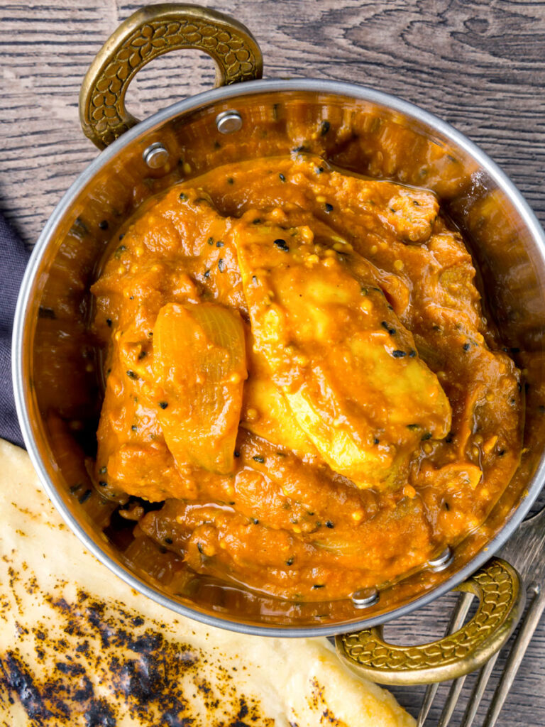 Portrait overhead image of a chicken jalfrezi curry served in a tarnished copper covered karahi bowl