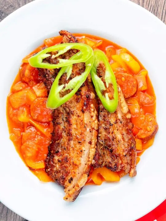 Portrait overhead image of a pork belly slices served on a hungarian tomato and pepper stew with salami and bacon