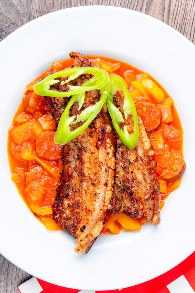 Portrait overhead image of a pork belly slices served on a hungarian tomato and pepper stew with salami and bacon