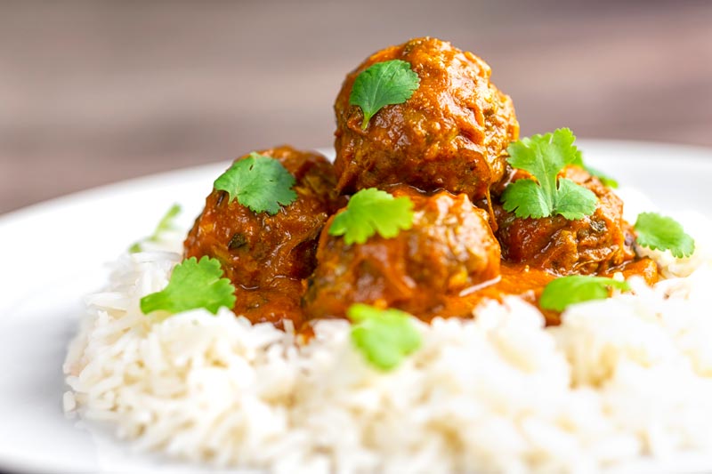 Landscape image of spicy venison meatballs served with basmati rice and coriander leaved