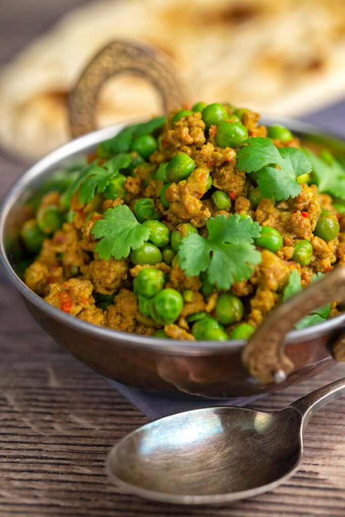 Portrait image of a keema matar minced lamb and pea curry serfved with coriander leaves in a karahi bowl