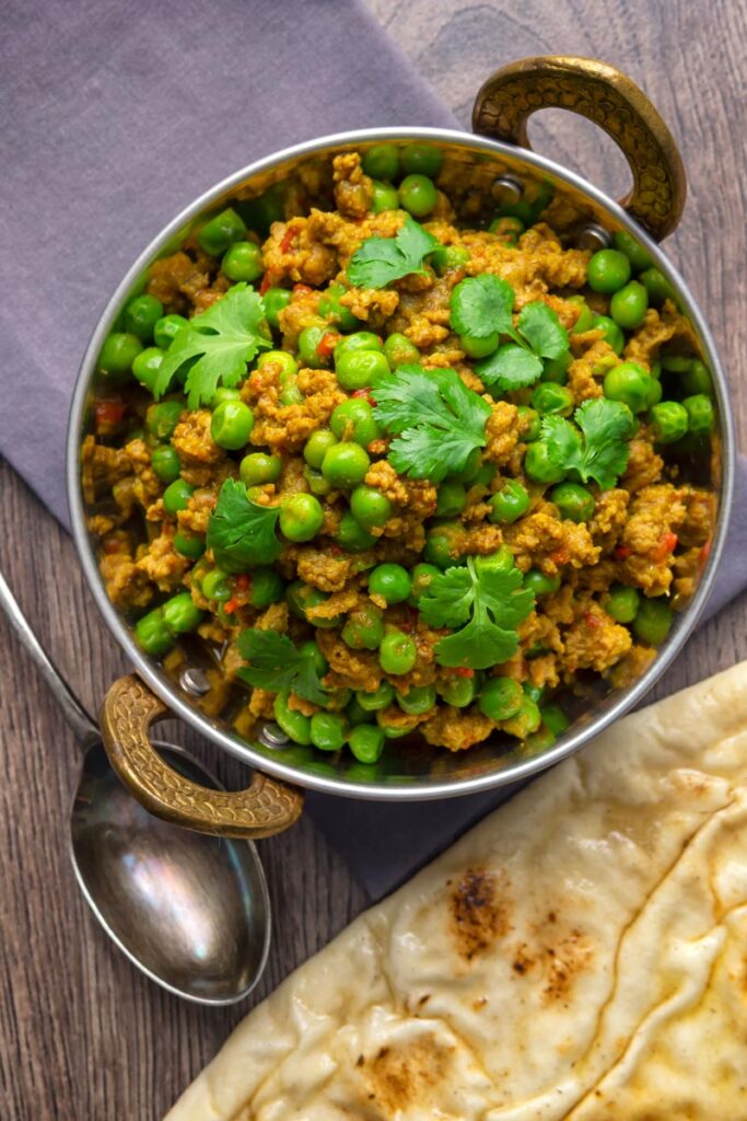 Portrait overhead image of a keema matar minced lamb and pea curry serfved with coriander leaves in a karahi bowl