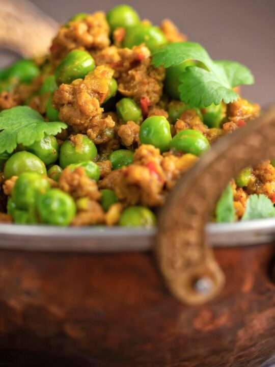 Portrait close up image of a keema matar minced lamb and pea curry served with coriander leaves in a karahi bowl