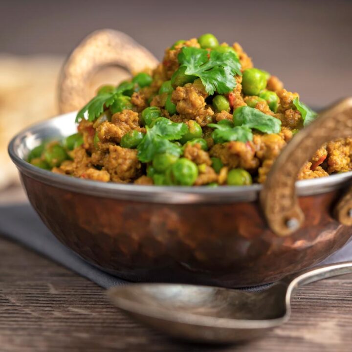 Square image of a keema matar minced lamb and pea curry served with coriander leaves in a karahi bowl