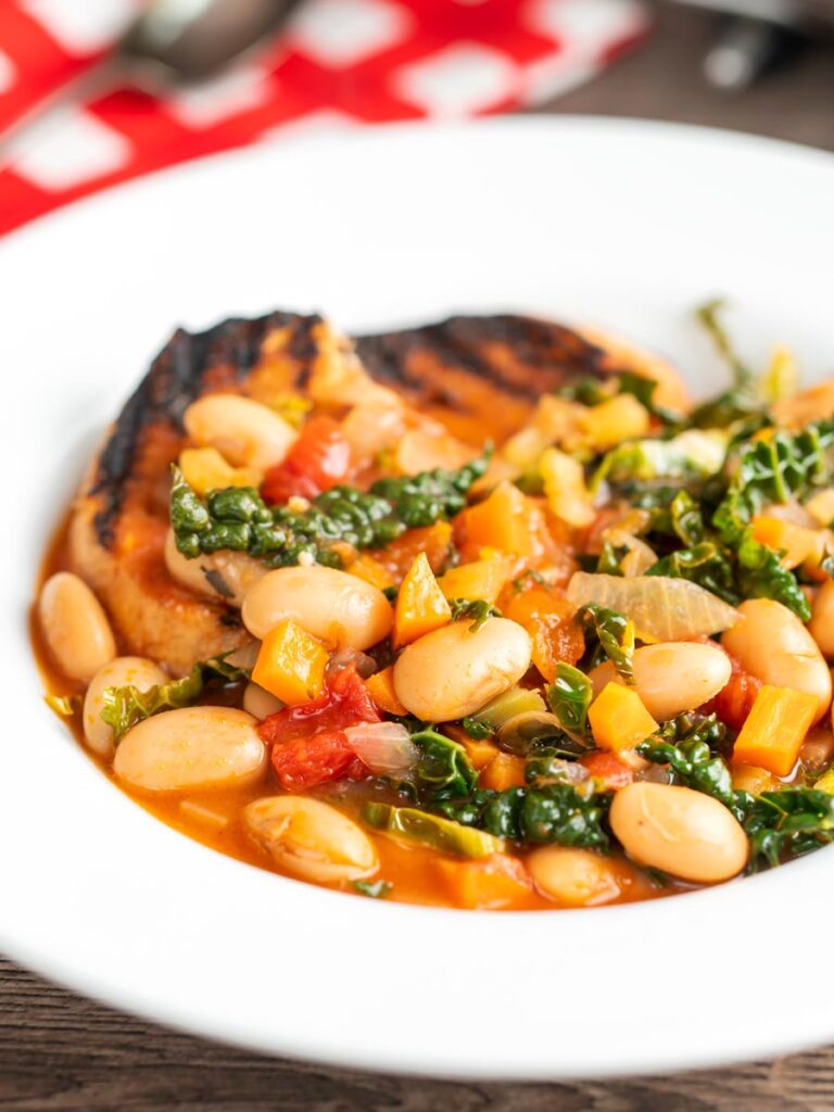 Portrait image of an Italian Ribollita stew featuring beans, cabbage, carrots, tomatoes and grilled bread