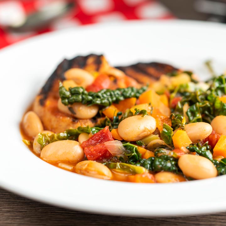 Square image of an Italian Ribollita stew featuring beans, cabbage, carrots, tomatoes and grilled bread