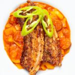 Portrait overhead image of roast pork belly slices served on a Hungarian lecso served in a white bowl