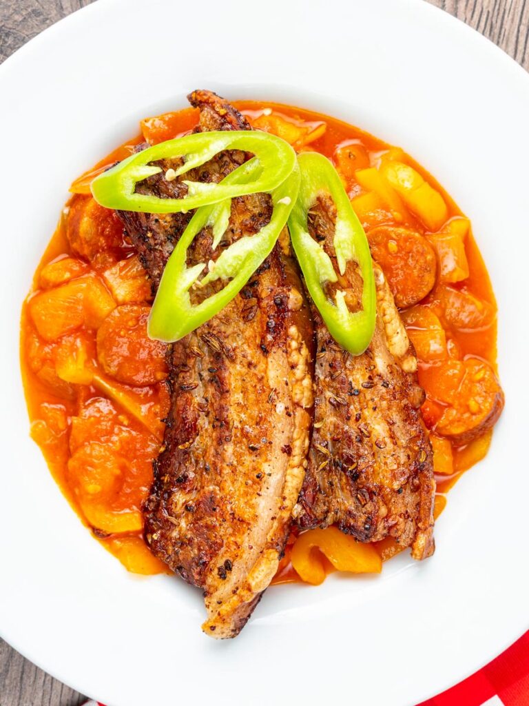 Portrait overhead image of roast pork belly slices served on a Hungarian lecso served in a white bowl
