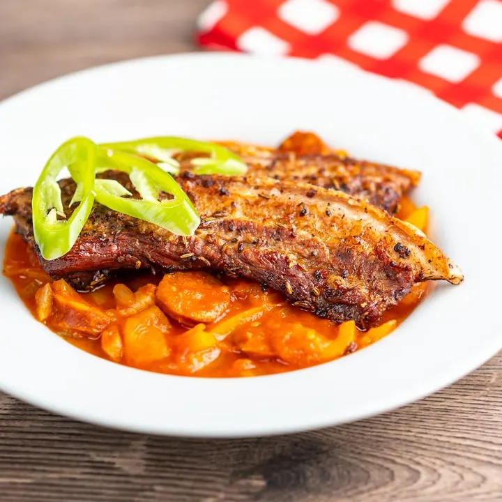 Square image of roast pork belly slices served on a Hungarian lecso served in a white bowl