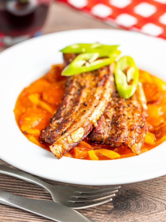 Portrait image of pork belly slices served on a Hungarian lecso served in a white bowl