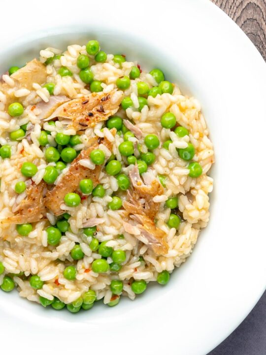 Portrait overhead image of a smoked fish risotto with peas served in a shallow white bowl