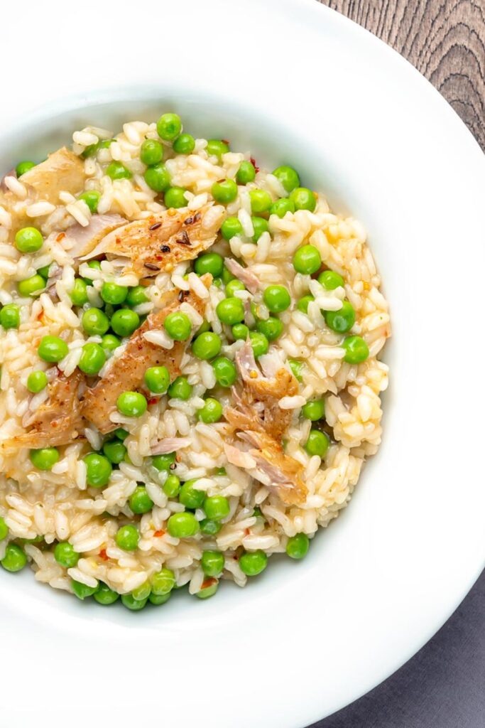 Portrait overhead image of a smoked fish risotto with peas served in a shallow white bowl