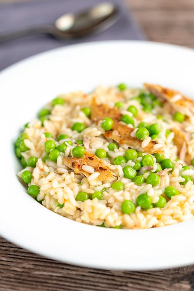 Portrait image of a smoked fish risotto with peas served in a shallow white bowl